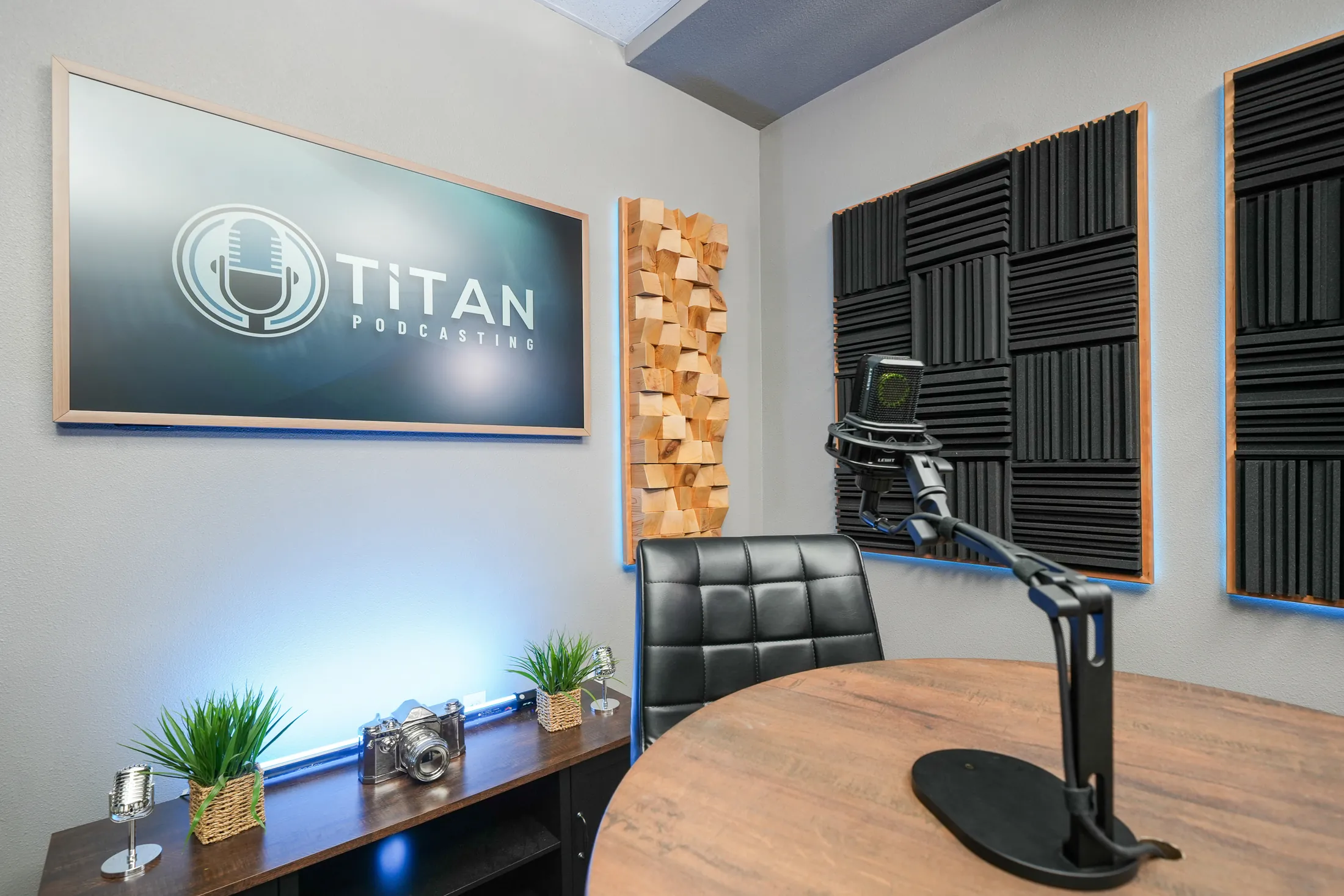 Titan Podcasting branding monitor, microphone, acoustic treatment, and blue set lighting